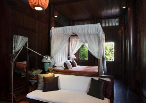 1 dormitorio con cama con dosel y sofá blanco en Chakrabongse Villas, en Bangkok