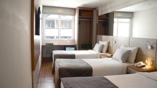 a hotel room with two beds and a desk at Hotel Atlântico Travel Copacabana in Rio de Janeiro