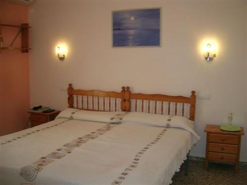a bed in a bedroom with two lights on the wall at Pensi&oacute;n Las Tres Golondrinas in Es Figueral Beach