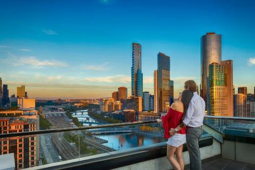 um casal em pé no topo de um edifício com vista para uma cidade em Aura on Flinders Serviced Apartments em Melbourne
