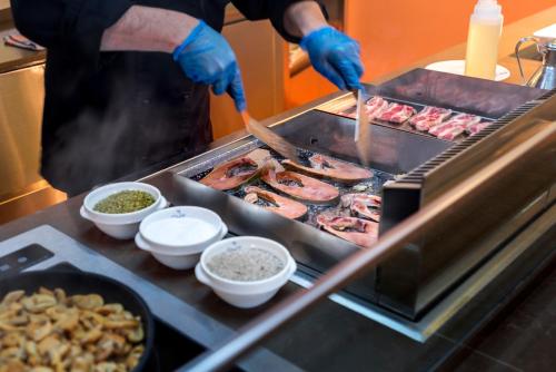 a person cooking food on a grill with tongs at GHT Balmes, Hotel-Aparthotel&SPLASH in Calella