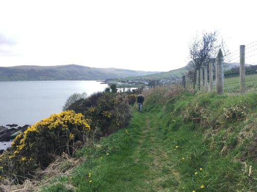 a man walking down a path next to a body of water at Ballymacdoe Cottage Cushendall in Cushendall