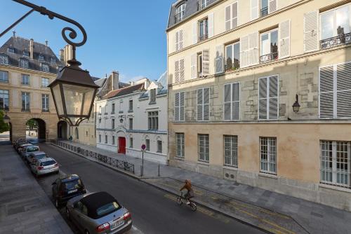 a person riding a bike down a street with buildings at Le Pavillon de la Reine & Spa, Place des Vosges in Paris