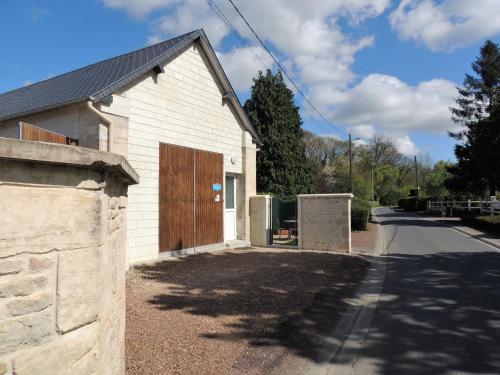 - un bâtiment blanc avec une porte en bois à côté d'une route dans l'établissement le petit Vauquelin, à Sommervieu