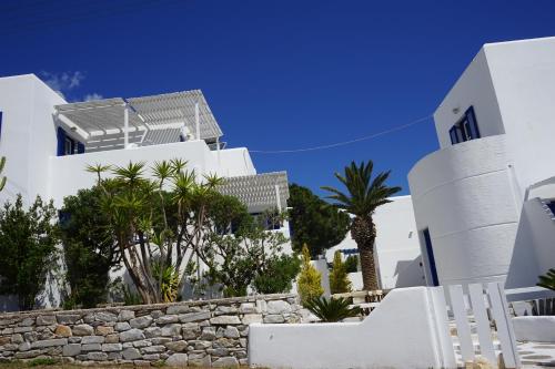 a white house with palm trees and a stone wall at Nicos Studios & Apartments in Logaras