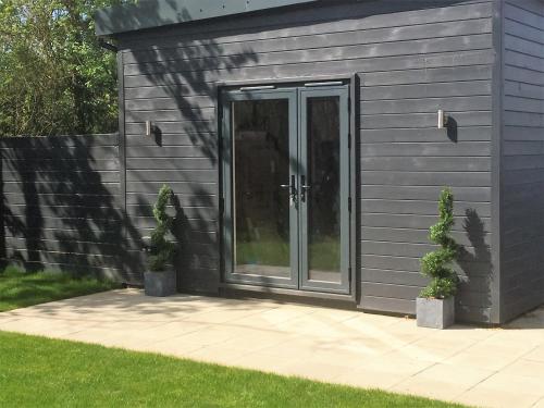 a gray shed with a glass door and two plants at Willow Court Farm Studio South & Petting Farm, 8 mins from Legoland & Windsor, 15 mins from Lapland UK in Windsor