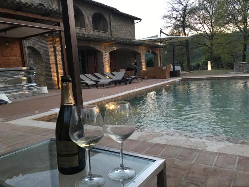 dos copas de vino sentadas en una mesa junto a una piscina en Villa valtopina, en Valtopina