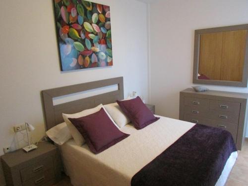 Un dormitorio con una cama con almohadas moradas y una pintura en Jovia Vacacional El Cotillo, en Cotillo