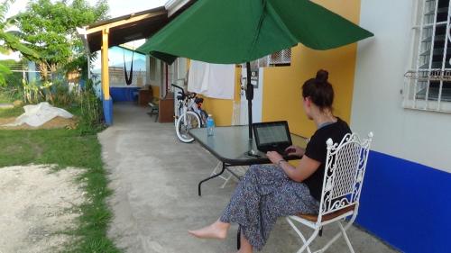 a woman sitting at a table with a laptop at Hacienda Tropical Guest House in Belmopan