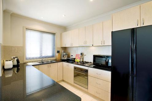 a kitchen with white cabinets and a black refrigerator at Pension Grimus Zurs Suite in Mount Buller