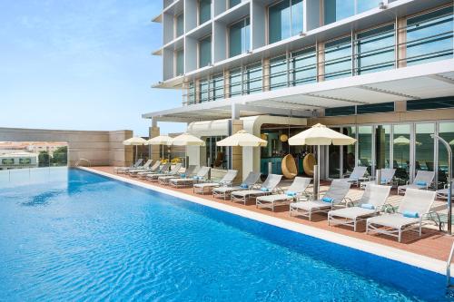 a swimming pool with chairs and umbrellas next to a building at Novotel Abu Dhabi Al Bustan in Abu Dhabi