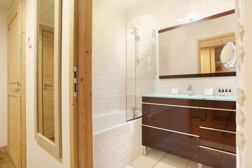 a bathroom with a tub and a sink and a mirror at Hôtel Prestige Odalys Le Chamois in La Clusaz