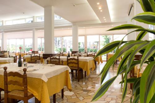 un ristorante con tavoli, sedie e una pianta di Hotel San Marco a Lignano Sabbiadoro