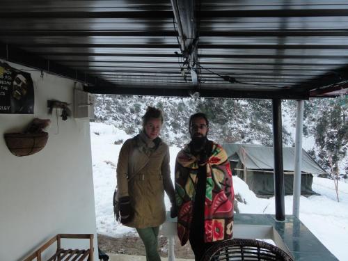 two people are standing under a building in the snow at Dhanaulti Camp Homes Retreat in Dhanaulti