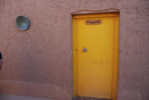 a yellow door on a pink wall with a sign on it at d'hôte Jnane-Dar Diafa in Tamegroute