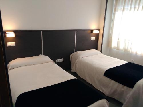 two beds in a hotel room with a window at Hostal Doña Isabel in Majadahonda