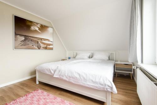 ein Schlafzimmer mit einem weißen Bett und einem Gemälde an der Wand in der Unterkunft Haus am Meer-Ferienwohnungen Sylt in Hörnum
