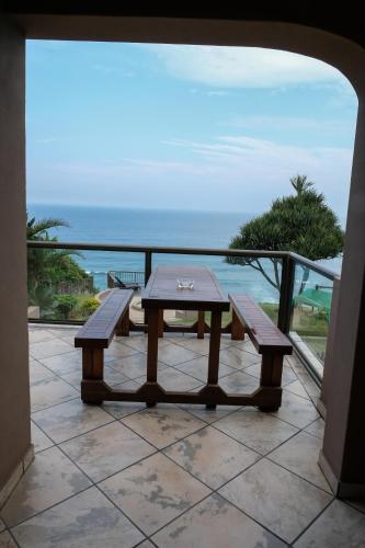 a table and benches on a balcony with the ocean at Beach Retreat Guesthouse in Amanzimtoti