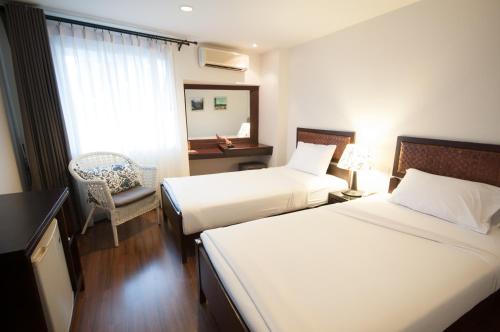 a hotel room with two beds and a chair at Kasemsarn Hotel Chanthaburi in Chanthaburi