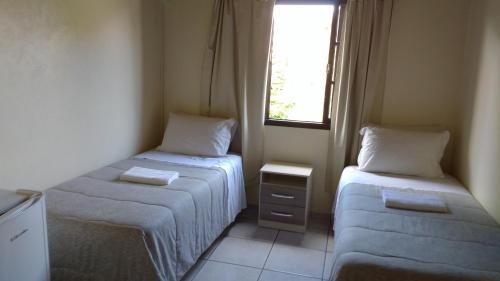 a small room with two beds and a window at Hospedaria Ondas do Rosa in Praia do Rosa