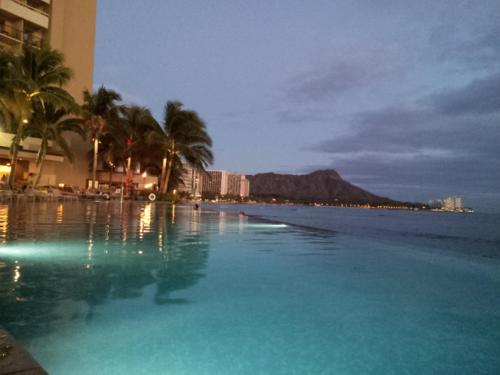 a swimming pool with a view of the ocean at night at Waikiki Shore Beachfront in Honolulu