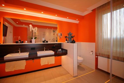 an orange bathroom with two sinks and a toilet at Hotel Modena in Bad Steben