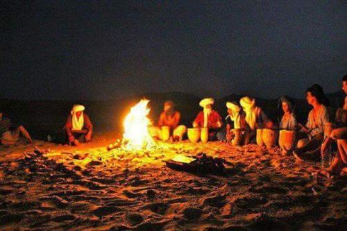 a group of people sitting around a fire on the beach at berber sahara in Zagora