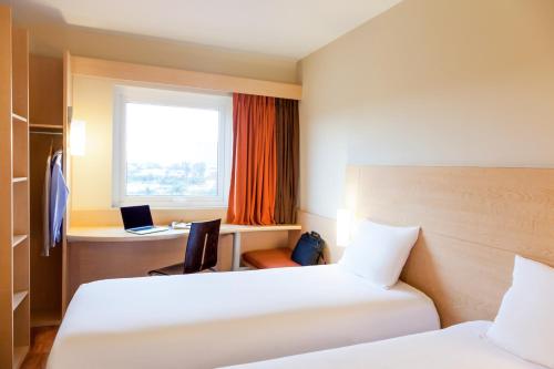 a hotel room with two beds and a desk and a window at Ibis Aguascalientes Norte in Aguascalientes