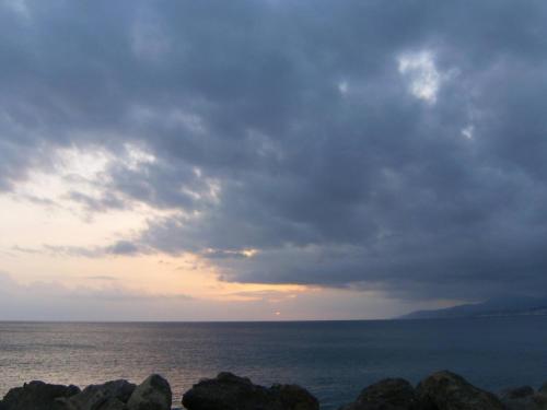 a cloudy sky over the ocean with rocks in the foreground at Εmmi in Koutsounari
