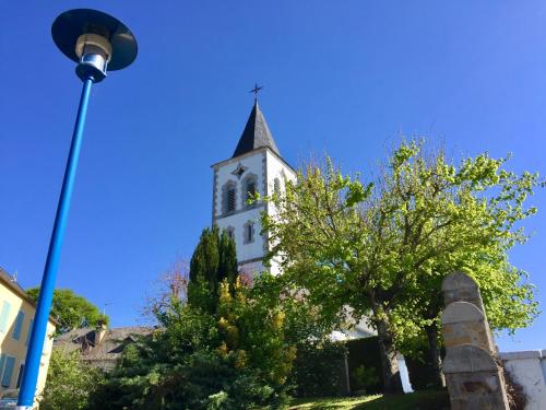 a church with a steeple with a tree and a street light at Les Gîtes de La Maison Bleue d'Estialescq in Estialescq