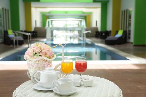 a table with two drinks and a basket of flowers and a pool at MaxOneHotels at Resort Makassar in Makassar