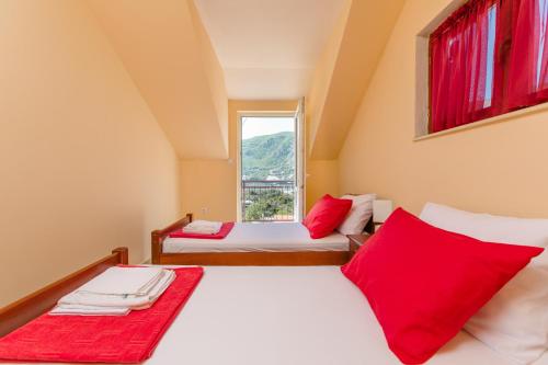 two beds in a room with red pillows and a window at Apartments Feniks in Kotor