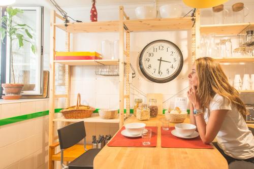 a woman sitting at a table with a clock on the wall at Lisbon Story Guesthouse in Lisbon
