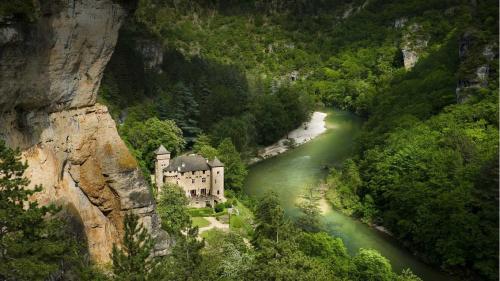 ein Gebäude an der Seite eines Berges neben einem Fluss in der Unterkunft Chateau De La Caze in Sainte-Énimie