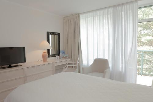 a white bedroom with a bed and a tv and a window at Hotel Bryza Resort & Spa in Jurata