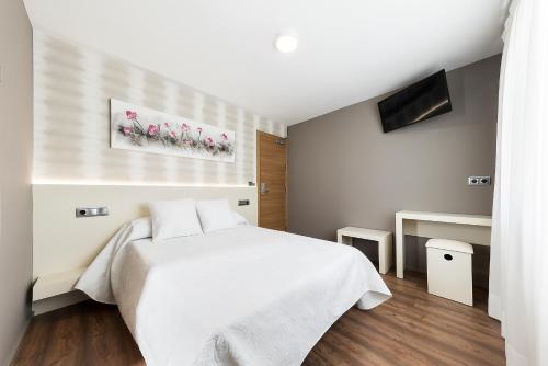 a white bedroom with a white bed and a television at Pension Residencial Victoria in Santa Cruz de Ribadulla