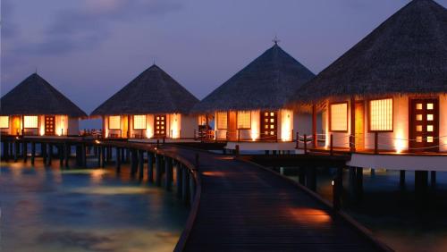 a row of houses on the water at night at Adaaran Prestige Water Villas - with Dine around Premium All inclusive - 24 hours in Raa Atoll