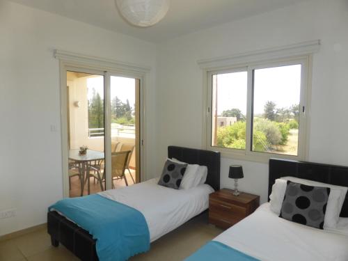 a bedroom with two beds and a table and windows at Aphrodite Sands Apartment D104 in Mandria