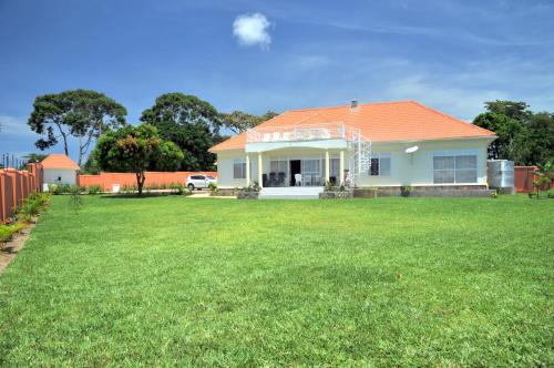a white house with an orange roof on a yard at Victoria Lake View Guesthouse & Safaris in Entebbe