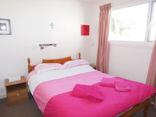 a bedroom with a bed with pink sheets and a window at Villa 44 in Camelford
