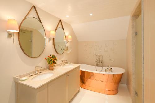 a bathroom with a tub and a sink and a mirror at Coworth Park - Dorchester Collection in Ascot