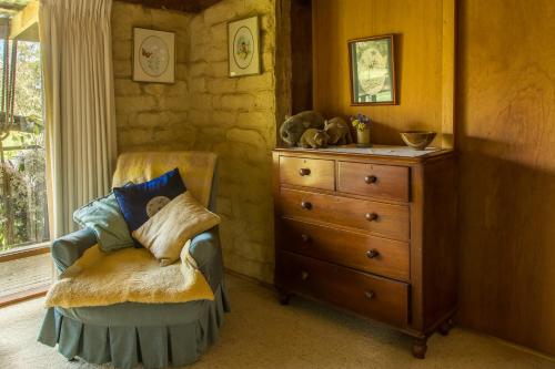 a bedroom with a dresser and a chair with pillows at The Burrow at Wombat Bend in Dixons Creek