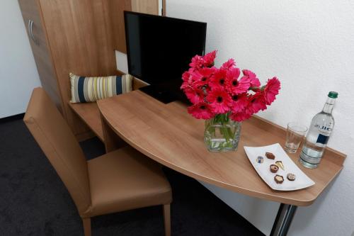 a desk with a vase of flowers and a bottle of wine at Hotel zwei&vierzig in Vallendar