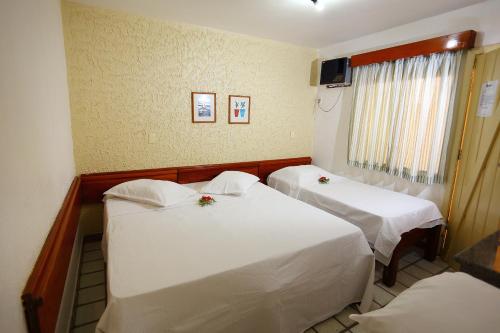 two beds in a hotel room with white sheets at Marlim Porto Hotel in Porto Seguro