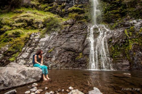 a woman sitting on a rock in front of a waterfall at Hotel Altiplanico Cajón del Maipo in San José de Maipo