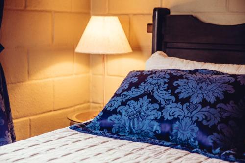a bed with a blue and white pillow and a lamp at Pousada Camelot Inn in Alto Paraíso de Goiás
