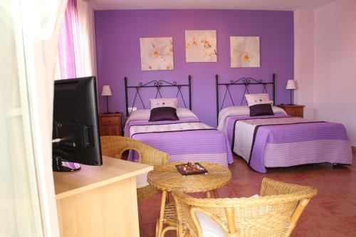 Habitación púrpura con 2 camas y mesa con TV. en Hostal Zaguan, en Talaveruela