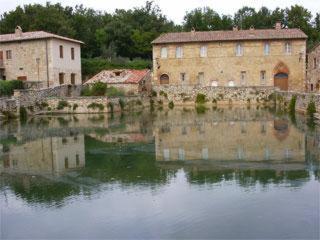 a reflection of two buildings in a body of water at La Locanda del Loggiato in Bagno Vignoni