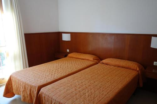 een slaapkamer met 2 bedden met oranje dekens en een raam bij Apartamentos Port-Pelegri in Calella de Palafrugell
