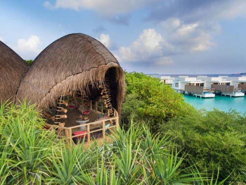 a resort with a thatched roof on a hill next to the water at Dhigali Maldives - A Premium All-Inclusive Resort in Raa Atoll